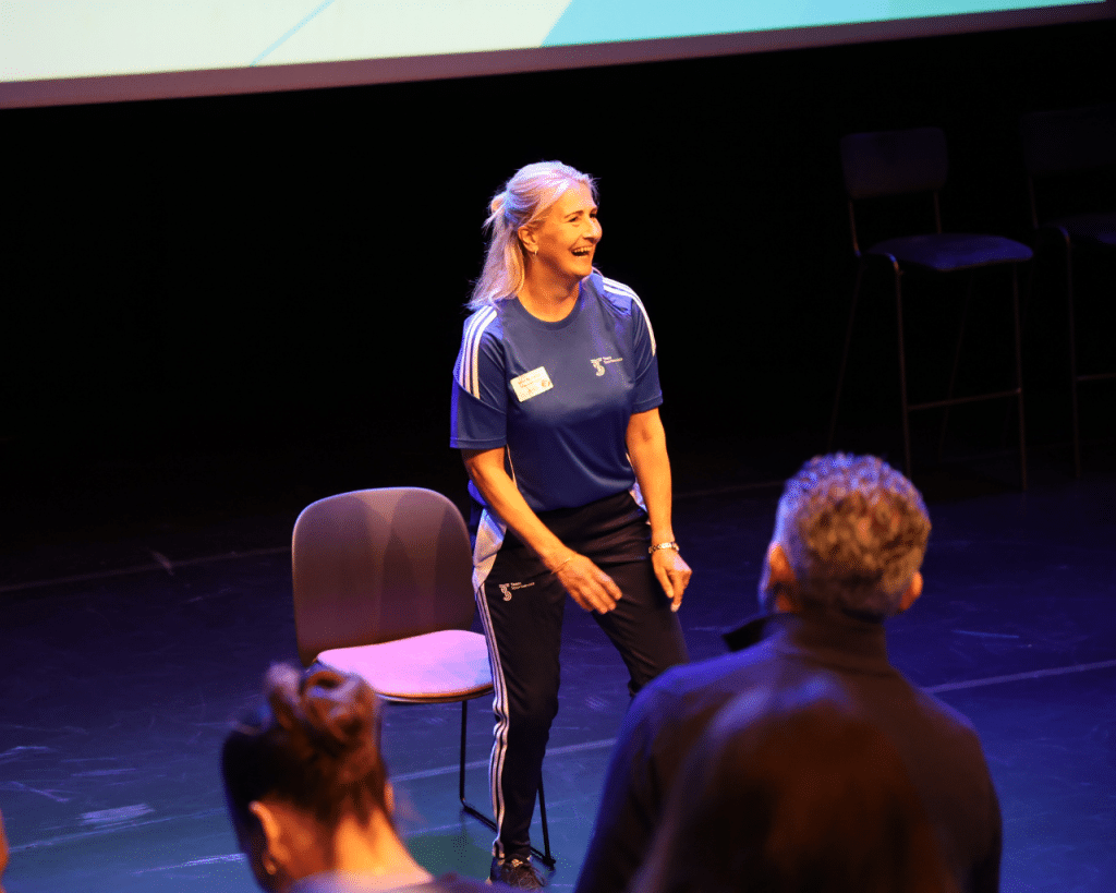 Wilma Raijmakers lachend voor de grote zaal tijdens haar beweegmoment