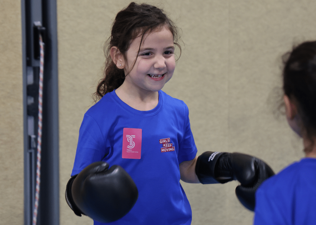 Meisje lachend in een blauw girls keep moving shirt met bokshandschoenen aan